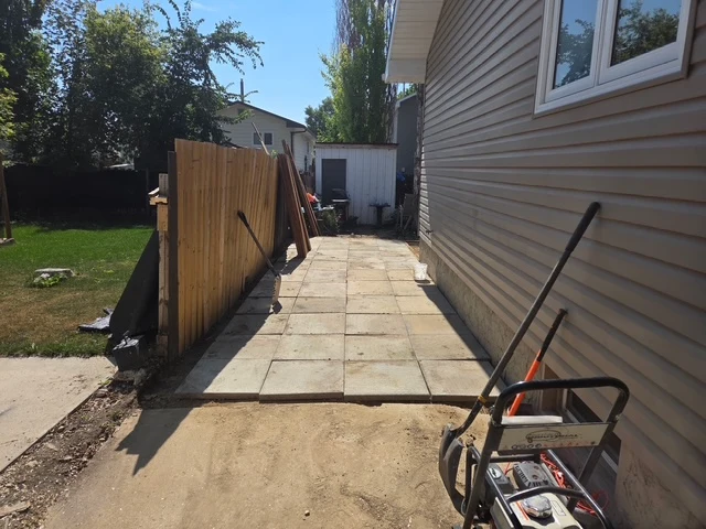 Paver walkway being laid along a side yard with fence panels staged, Regina SK